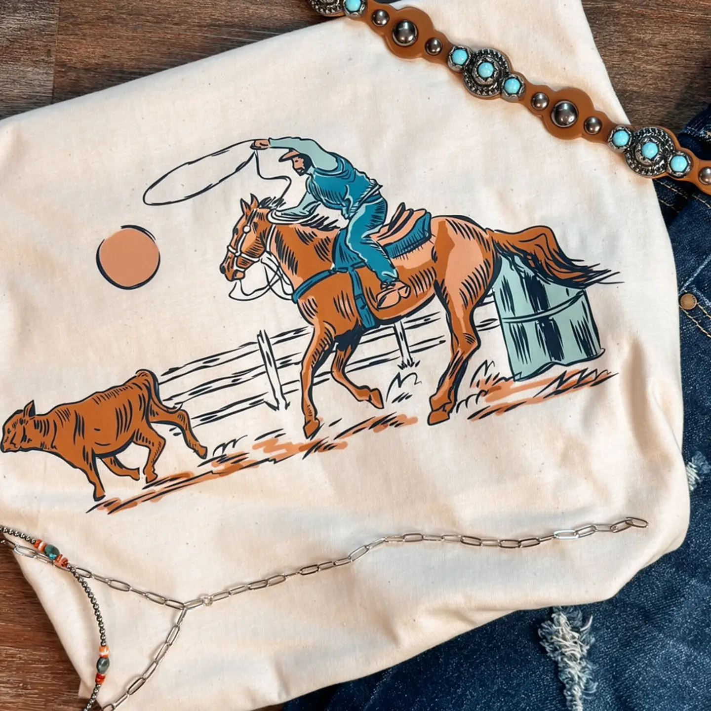 Cream Rodeo graphic tee featuring a cowboy, horse and calf